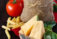 Ingredients for preparing pasta. Cheese, tomatoes, basil and pasta in a bag on a dark wooden background.