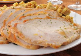 A platter of sliced turkey on top of herbal stuffing